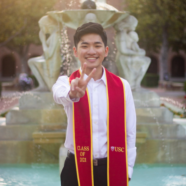 Justin dressed up in his graduation sash posing with a 'Fight on!' sign.